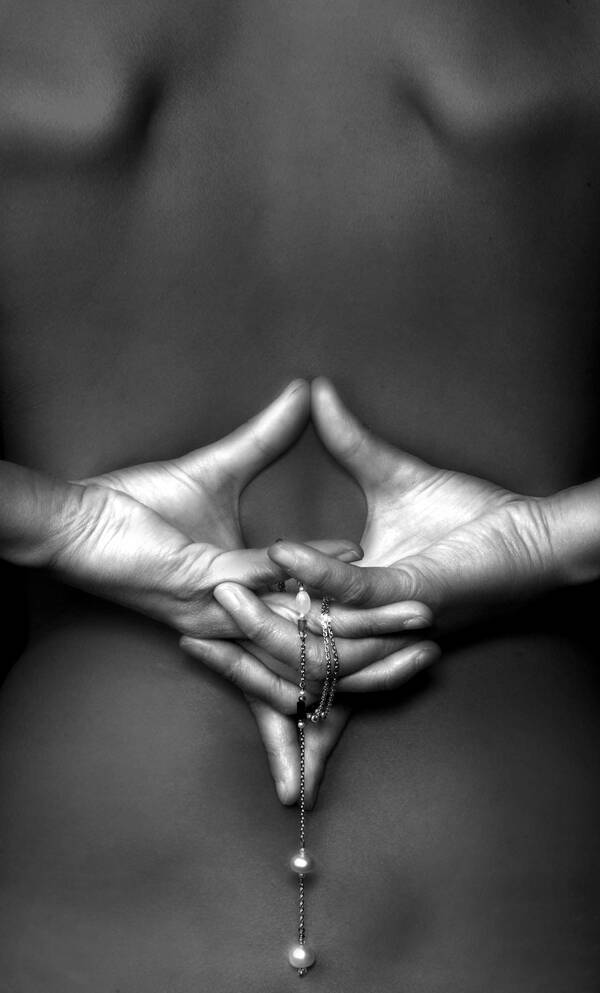 Ein Mensch hält die beiden Hände so hinter seinem nackten Rücken, dass die Finger ineinander verschränkt sind, die beiden Daumen nach oben und die beiden Zeigefinger nach unten zeigen. Die Hände halten eine Kette mit Perlen. Schwarz-Weiß.