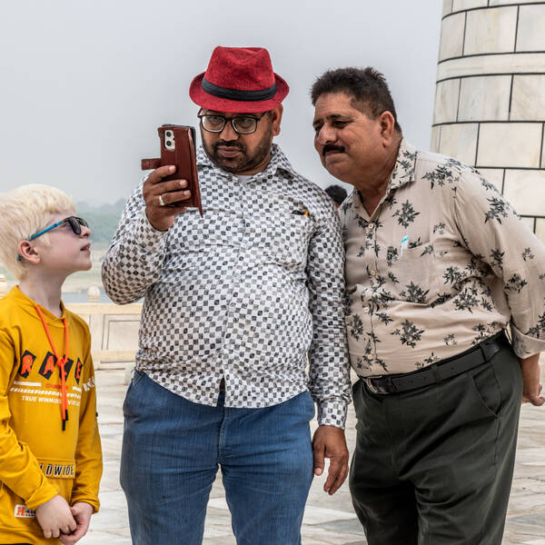 Zwei Männer schauen auf ein Smartphone, ein blonder Bub mit Sonnenbrille versucht auch einen Blick auf das TElefon zu erhaschen.
