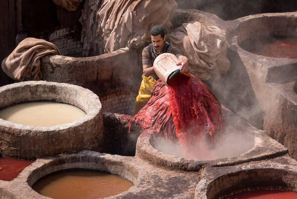 Ein Färber gießt rote Farbe in einen von vielen steinernen Tröge.