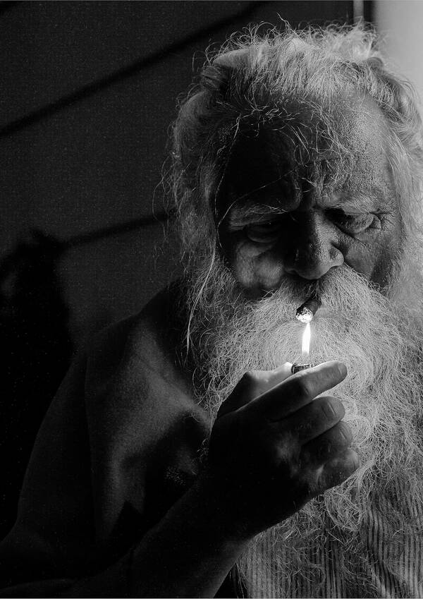 Ein weißhaariger Mann mit Rauschebart zündet sich eine Toscano an. Schwarz-Weiß.