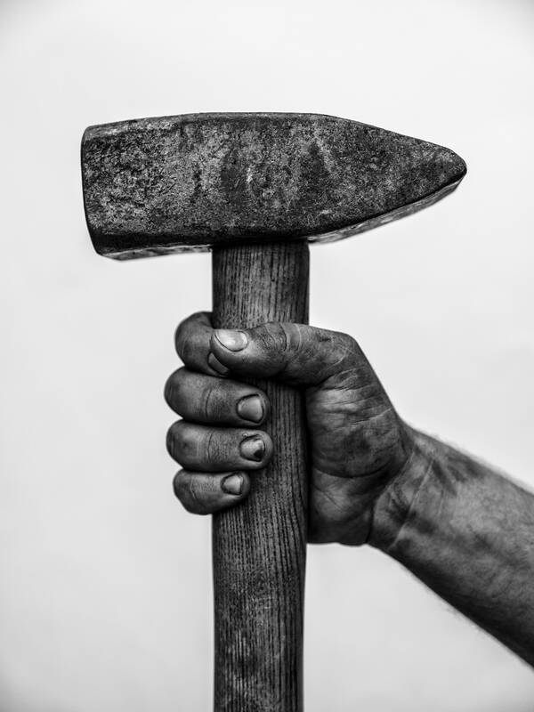 Eine schmutzige Hand hält einen schweren Hammer. Schwarz-Weiß.