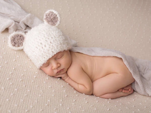 Ein Baby schläft mit einer weißen Wollmütze mit zwei runden Ohren.