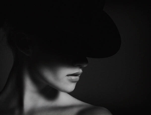 Portrait einer jungen Frau, deren obere Gesichtshälfte von einem Hut verdeckt wird. Schwarz-Weiß.