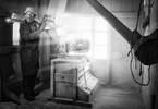 Ein Mann in Arbeitskleidung und Schutzbrille steht an einer alten motorbetriebenen Getreidemühle, Schwarz-Weiß