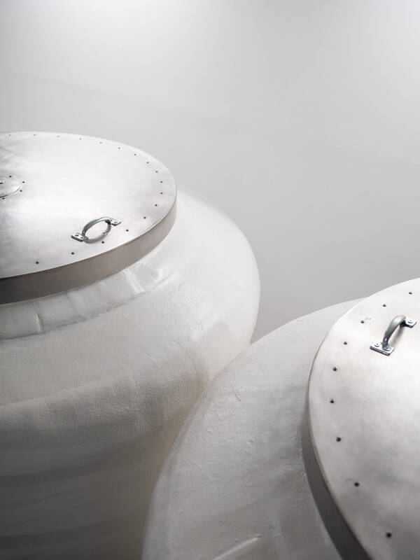 Zwei große, weiße, gemauerte Gefäße mit Stahldeckeln mit Griffen.