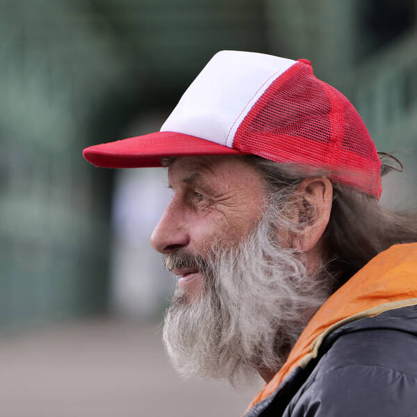 Profil-Portrait eines alten Mannes mit grauem Bart und einer rot-weißen Schirmkappe.