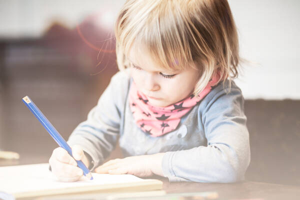 Ein Mädchen sitzt an einem Tisch und malt mit einem großen blauen Stift.