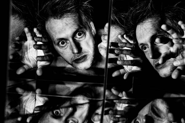 Portrait eines Mannes, der in einen verspiegelten Würfel schaut. Schwarz-Weiß.