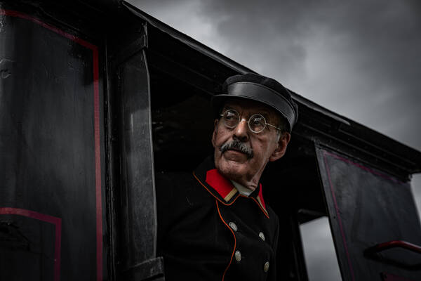 Ein Zugbegleiter in historischer Uniform schaut aus einer alten Dampflock.