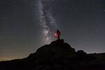 Silhouette eines Menschen, der auf einer Bergspitze die Milchstraße fotografiert.