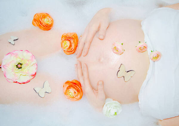 Bauch einer Schwangeren in einem Schaumbad mit Blüten und hölzernen Schmetterlingen dekoriert.