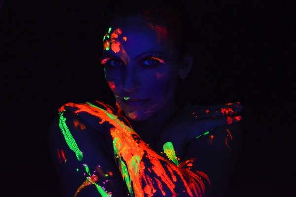 Eine Frau im Dunkeln, bemalt mit Farben, die im UV-Licht neonfarben leuchten.
