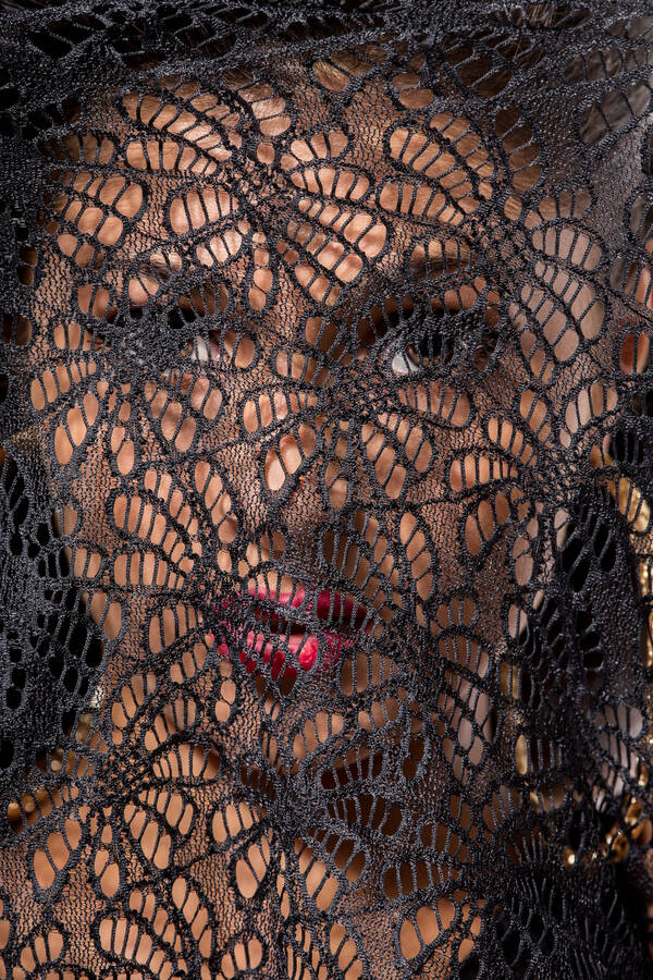 Portrait einer Frau hinter einem schwarzen, stark strukturiereten, schleierartigen Tuch.