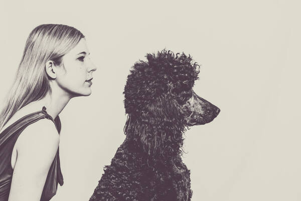 Eine junge Frau mit langen, glatten Haaren und ein gelockter Pudel beide im Profil. Schwarz-Weiß, getönt.