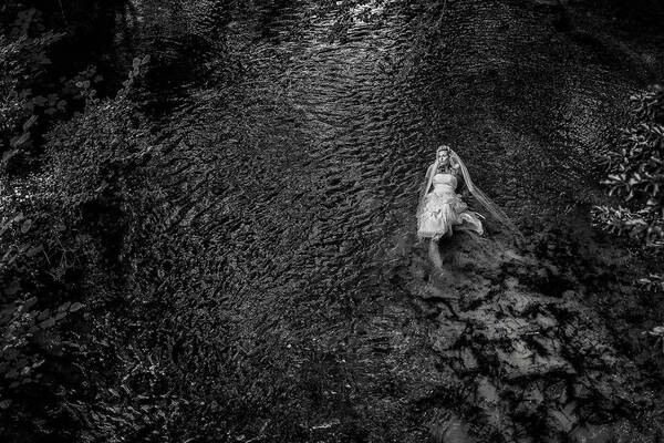 Eine Braut liegt mit Brautkleid im dunklen Wasser. Schwarz-Weiß.