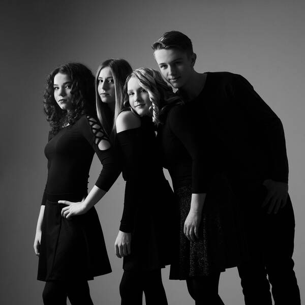 Gruppe von vier Teenagern – drei Mädchen, ein Bursche – in eleganten, dunklen Gewändern. Schwarz-Weiß.