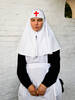 Frau in Ordenstracht mit rotem Kreuz auf dem Kopftuch vor weiß getünchter Ziegelwand.