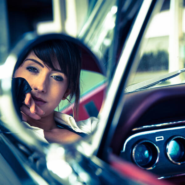 Portrait einer jungen Frau im Rückspielgel eines Vintage-Wagens.
