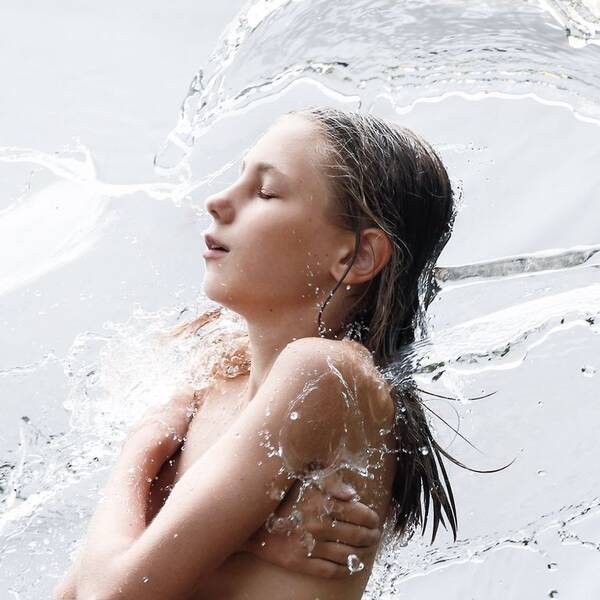 Eine nackte junge Frau wird von einem Wasserschwall getroffen.