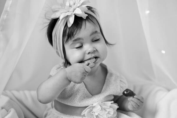 Ein Kleinkind mit Blumen-Stirnband isst ein Keks. Schwarz-Weiß.