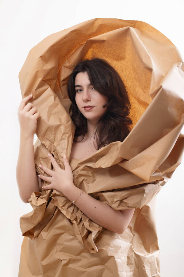Portrait einer jungen Frau, ganz in braunes Packpapier gehüllt, das um Ihren Kopf herum wie eine Calla-Blüte geformt ist.