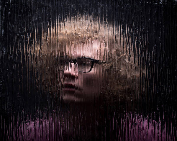 Portrait einer Person mit dunkler Brille durch eine geriffelte Glasscheibe hindurch.