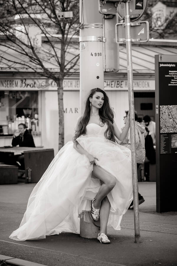 Eine junge Frau in Brautkleid und Sneakers lehnt sich an einen Laternenpfahl am Jakominiplatz und hält sich an einem Verkehrsschild fest. Schwarz-Weiß