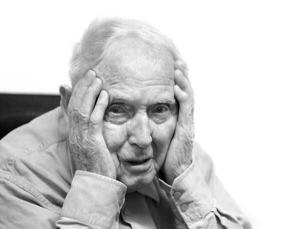 Ein alter Mann hält seinen Kopf in Händen. Schwarz-Weiß.