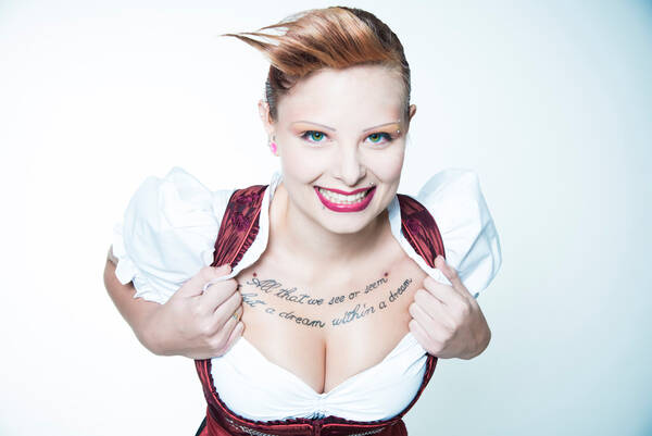 Portrait einer jungen Frau in einem Trachtenkleid, die offenherzig ihr Dekolletet präsentiert: oberhalb der Brüste hat sie ein Zitat von Edgar Allan Poe tätowiert: 