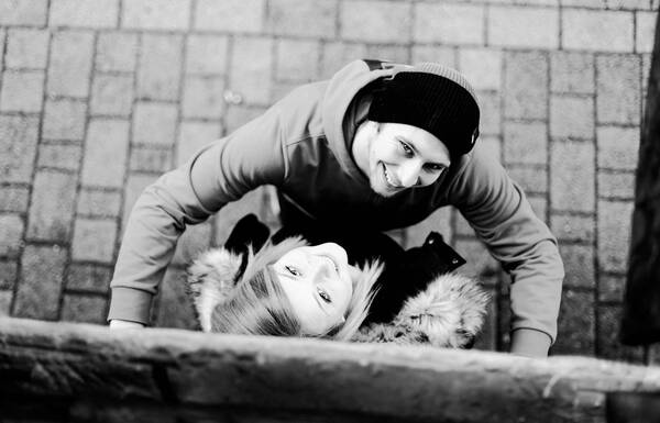 Aufnahme von oben von einem Paar: Sie lehnt an einer Wand, er stützt sich an dieser Wand mit den Händen links und rechts von ihr ab. Beide schauen nach oben in die Kamera. Schwarz-Weiß.