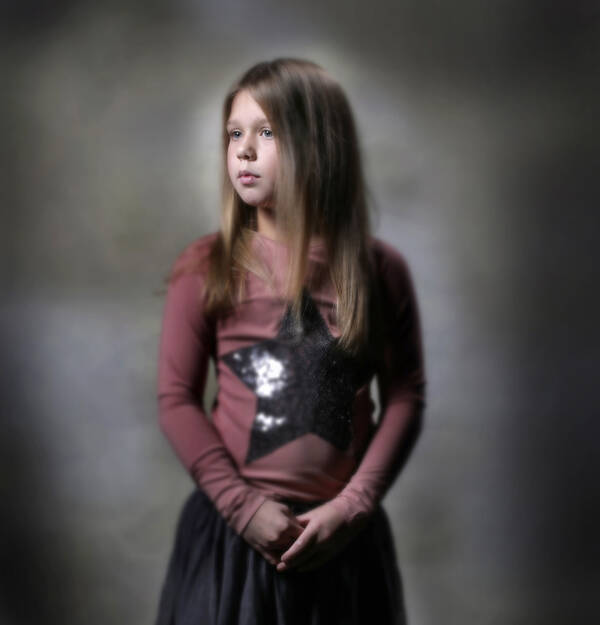 ein Mädchen in einem roten Shirt mit einem glitzernden Stern schaut verträumt aus dem Bild.