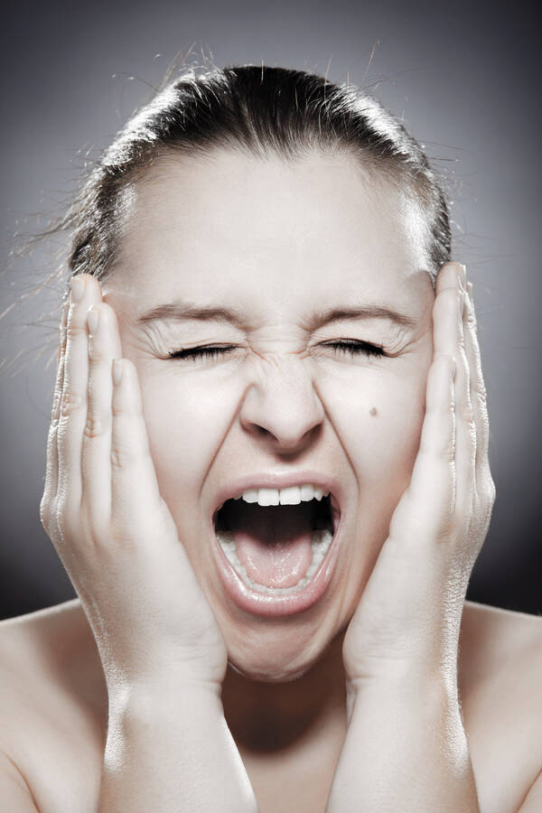 Portrait einer Frau, die die Hände ans Gesicht gelegt hat und schreit.