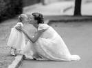 Eine Braut hat sich am Straßenrand hingehockerlt und gibt einem kleinen, ganz in weiß gekleideten Mäderl einen Kuss. Schwarz-Weiß.