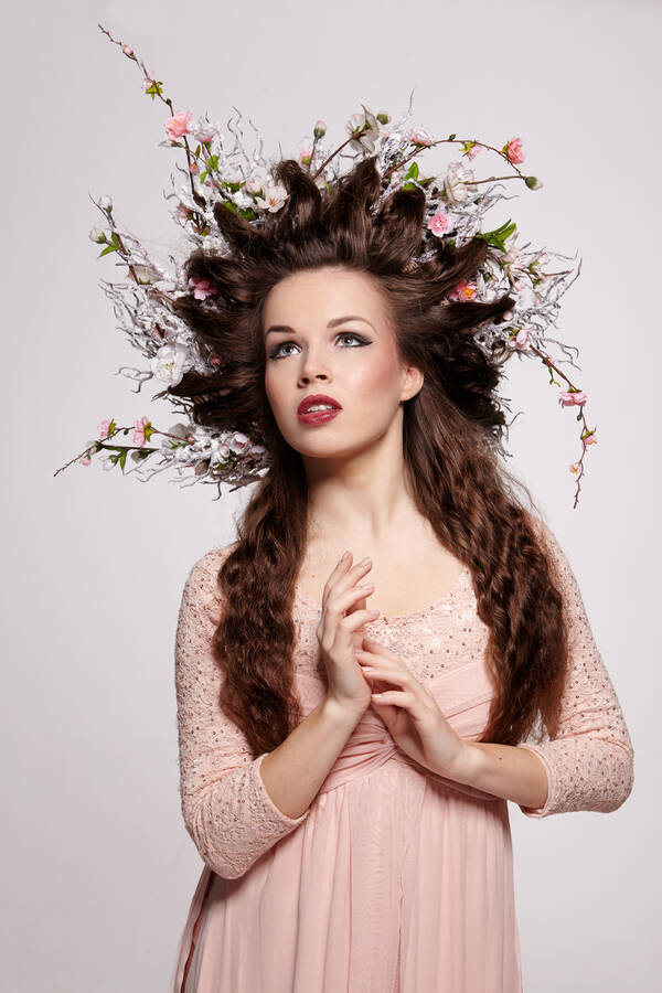 Portrait einer jungen Frau mit langen braunen lockigen Haaren und einem zartrosa Kleid. Die Haare sind mit Blütenzweigen geschmückt und zu einem Stern geformt.