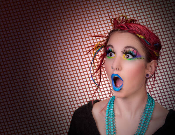 Portrait einer jungen, in grellen Farben geschminkten Frau mit bunten Haaren mit erstauntem Gesichtsausdruck.