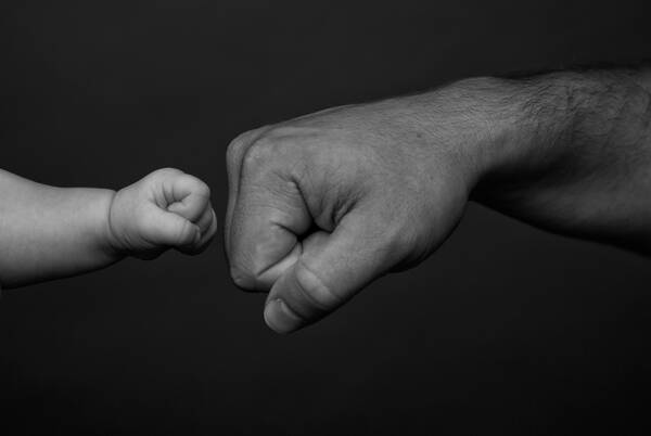 Die Faust eines Mannes und die Faust eines Babies begegnen sich. Schwarz-Weiß.