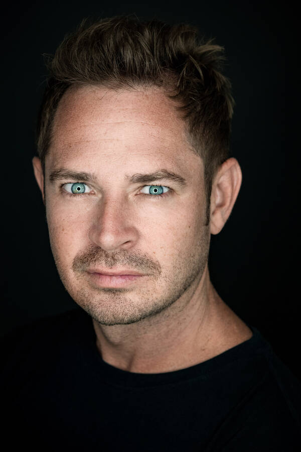 Portrait eines Mannes vor schwarzem Hintergrund. Der Ringblitz zeichnet feine weiße Kreislinien rund um die Pupillen.