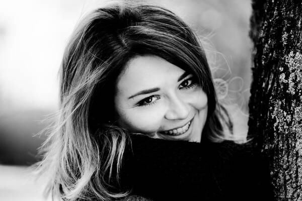 Portrait einer jungen Frau, die an einem Baum lehnt. Schwarz-Weiß.