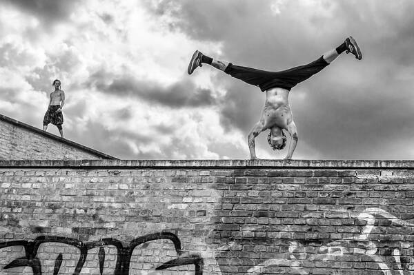Zwei Männer beim Parcour, einer macht auf einer Mauer einen Handstand. Schwarz-Weiß.