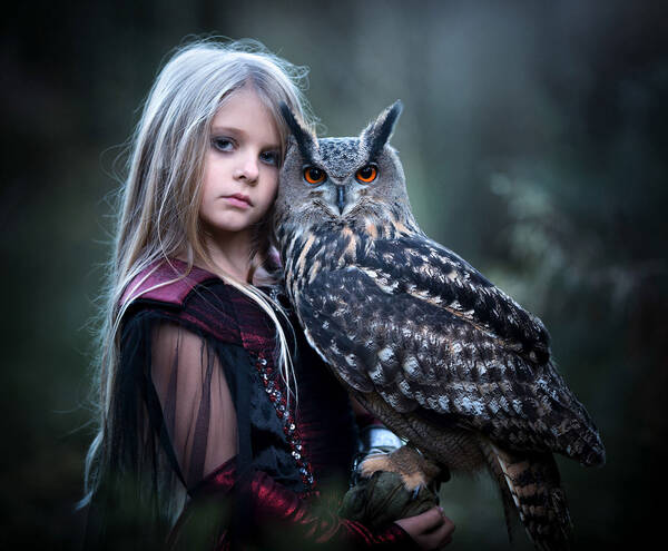 Ein junges Mädchen mit langen blonden Haaren trägt einen Uhu auf dem Arm.