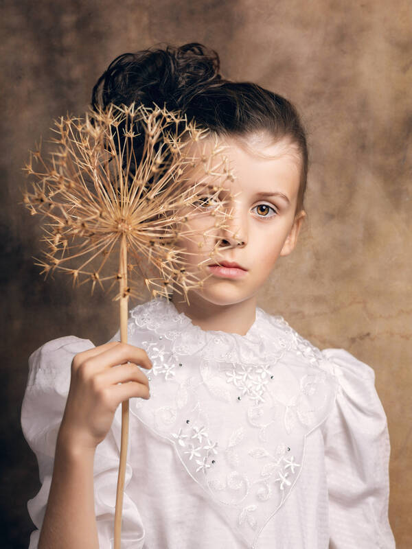 Portrait eines Mädchens in einer weißen Bluse mit aufgesteckten Haaren. In der rechten Hand hält es eine getrocknete Kugellauch-Blüte.
