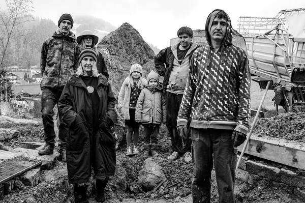 Sieben Menschen unterschiedlichen Alters und Geschlechtes – möglicherweise eine Familie über drei Generationen – stehen inmitten von landwirtschaftlichen Geräten. Schwarz-Weiß.