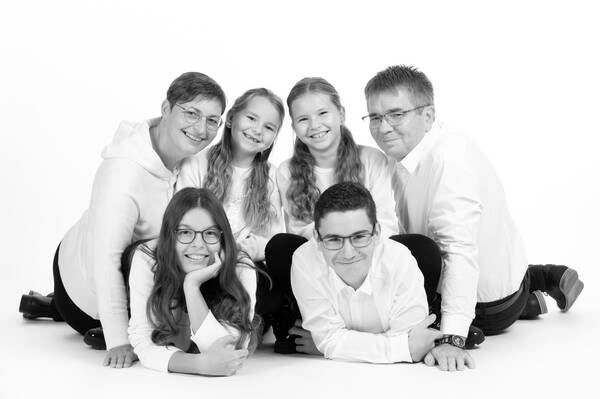 Eine Familie mit vier – zum Teil schon großen – Kindern liegt am Boden und sieht in die Kamera. Schwarz-Weiß