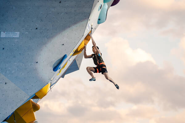Ein Sportkletterer an einer Kletterwand gegen den Himmel fotografiert.
