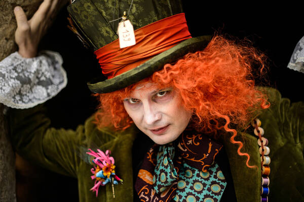 Ein Mann, kostümiert wie der Mad Hatter aus Alice im Wunderland, lehnt an einem Baum.