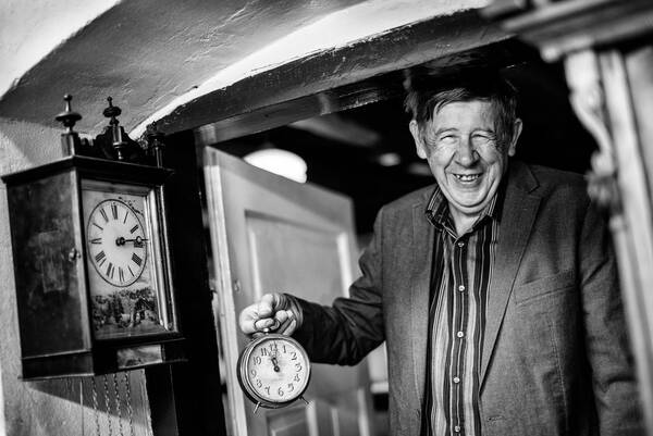 Ein älterer Mann steht im Türstock und hält eine alte Uhr in der Hand. Schwarz-Weiß.