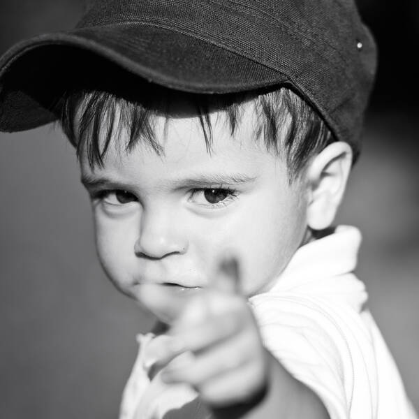 Ein Kind mit Baseball-Kappe schaut und zeigt in die Kamera. Schwarz-Weiß