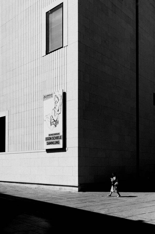 Eine Frau geht durch das Museumsquartier vor dem Leopold-Museum. Harte, dominierende Schatten, Schwarz-Weiß.