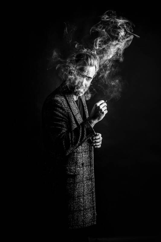 Low-key-Portrait eines Mannes in langem Mantel, der Raucht. Schwarz-Weiß. 