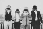 Vier Männer in eleganten Anzügen halten ihre Zilinder, bzw. den Hut so, dass ihre Gesichter verdeckt sind. Schwarz-Weiß.